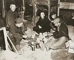 Five men sitting in a circle on the floor of a barracks
