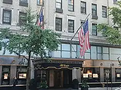 Entrance to the Cafe Carlyle and Bemelmans Bar. There is a marquee with the words "Cafe Carlyle", as well as two American flags, above the entrance.