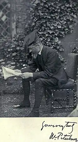 middle-aged man in Victorian ecclesiastical costume sitting reading in a garden