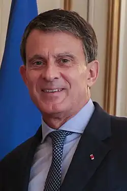 Headshot of Manuel Valls, a middle-aged man with short, salt and pepper hair, wearing a morning suit.