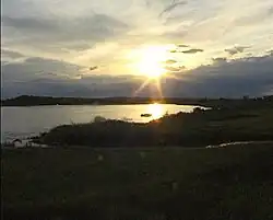 The sun low over the horizon over a body of water surrounded by dark vegetation