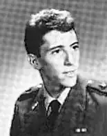 A man with his head turned left smiles slightly as his photograph is taken.