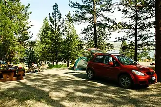 Campsite with a red car next to a tent in a small clearing surrounded by trees