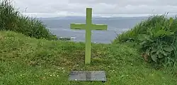Green cross on the cliff edge overlooking the sea. A stone tablet in front of it reads "In memory of all those who lost their lives or were touched by the Troubles. Including those who were on board Shadow V at sea on 27th August 1979 Nicholas Knatchbull ages 14, Paul Maxwell ages 15, Lord Louis Mountbatten aged 79 Lady Doreen Brabourne aged 83. Go ndéana Dia trócaire ar a nanamacha agus go bhfaighimíd go léir síochain in ar gcroíthe." The Gaelic translates as "May God have mercy on their souls and may we all find peace in our hearts".