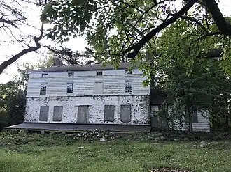 A photograph of a white abandoned house in an overgrown yard.