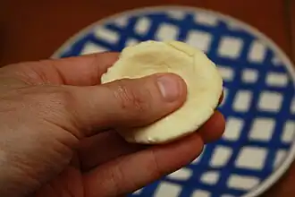 A small piece of dough being flattened in someone's hand