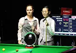 Two women holding snooker cues, standing at a snooker table