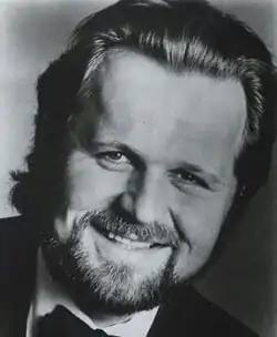 Black and white publicity shot of a smiling, bearded man, with greying hair brushed back.