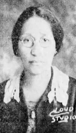 A Black woman with hair parted center and dressed to the nape, wearing round eyeglasses and a dark jacket with a lace-trimmed collar; the words "Cloud Studio" are legible in the lower right corner