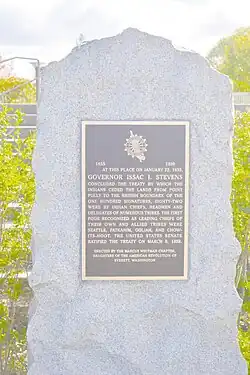 A bronze plaque with gold typeface, on a flat rectangular rock slab.