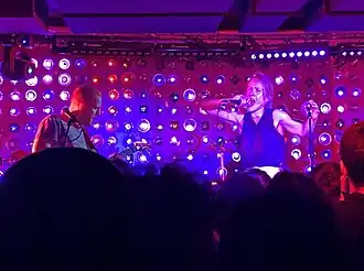 A singer and guitarist perform against a wall of purple and blue LED lights