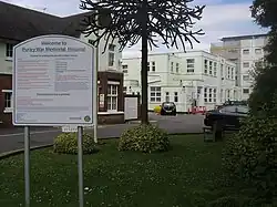 A picture of the entrance to the hospital, with a welcome sign in the foreground and the hospital buildings in the background.