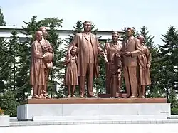 A Bronze statue of Kim Il Sung and six other people with a camera, a flower basket and a notebook.