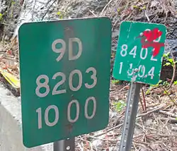 Two nearly adjacent markers, one slightly defaced with red ink, with slightly different sets of numbers