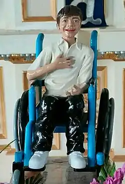 A statue of a smiling Ramos in a wheelchair, on a white background adorned gold lining