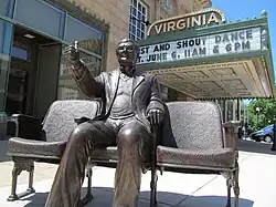A color photograph of a bronze statue of a seated man giving a thumbs up gestue