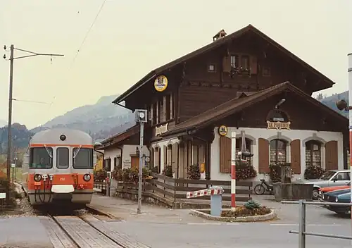 Three-story station building next to a single-line track with an orange train