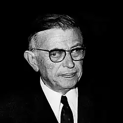 Black-and-white photo of a man with glasses wearing a dark suit with a tie