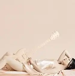 A mostly naked woman reclining, holding a Gibson SG guitar.