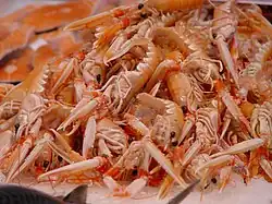 A heap of small pink lobsters on their sides, with their claws extended forwards towards the camera.