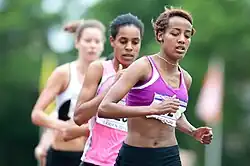 Three women running at a marathon, one in front of the other, Hassan in front.