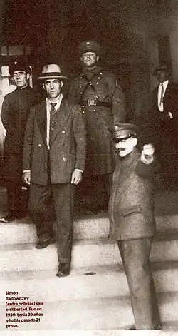 Photograph of Simon Radowitzky leaving prison in a pinstripe suit, while a guard points him the way