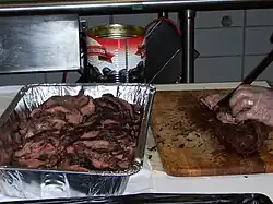 A member of the catering staff slices the pre-cooked beef loin into slices behind the scenes at a beefsteak