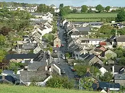 View from above of a village, with buildings clustered along a straight road heading into the distance. A small church is in the centre.