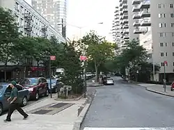 Looking east from Third Avenue along the median of 66th Street. There is a main roadway for through traffic on the left, as well as a service road for local traffic on the right. Manhattan House is on the right.