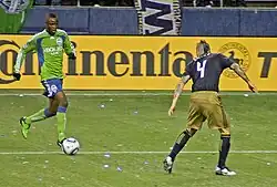 Zakuani dribbles towards an opposing player during a match