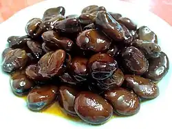 Shoyumame in a black color with juices dripping out of it onto a white plate.