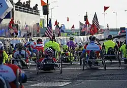 Multiple competitors in a mixture of high and low stance handcycles, all facing away from the camera.