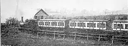 A black and white photograph showing a small train pulling into a small, rural railway station.