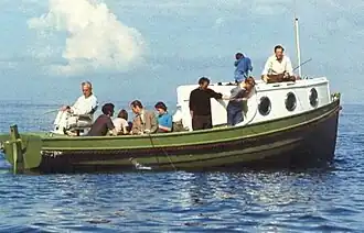 Small green and white cabin cruiser. Mountbatten is sitting at the stern and eight others are on deck
