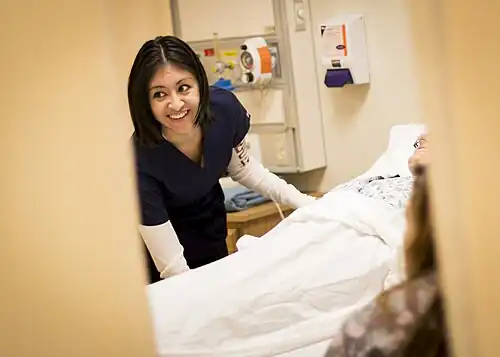 Smiling woman in scrubs leans over a hospital bed