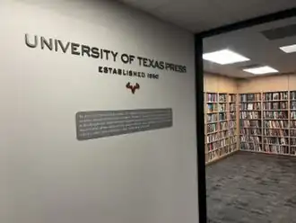 An image of the UT Press office, with its logo and title on the wall and a bookshelf in the background.