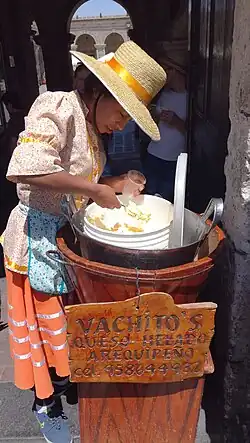 A woman serves queso helado out of a traditional wood and metal container.