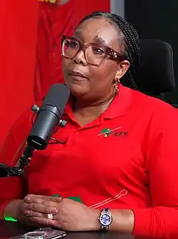 A woman seated at a table and behind a microphone, wearing a red polo shirt