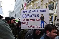 A protester holding a placard that states "Making good people defenceless won't make bad people harmless"