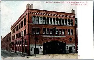 Postcard view of a three-story brick building. Streetcar tracks enter a large arch on the first story.