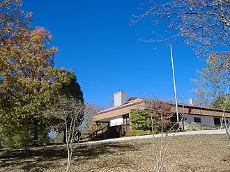 The visitor center is depicted as a building on a hill, surrounded by trees with autumn foliage and a clear blue sky.