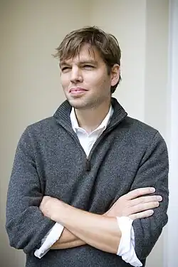 Johnson in a gray sweater and crossing his arms.