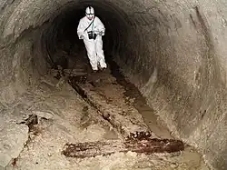 Photograph of a man in white overalls in a tunnel with an 1880s tunnel bore.