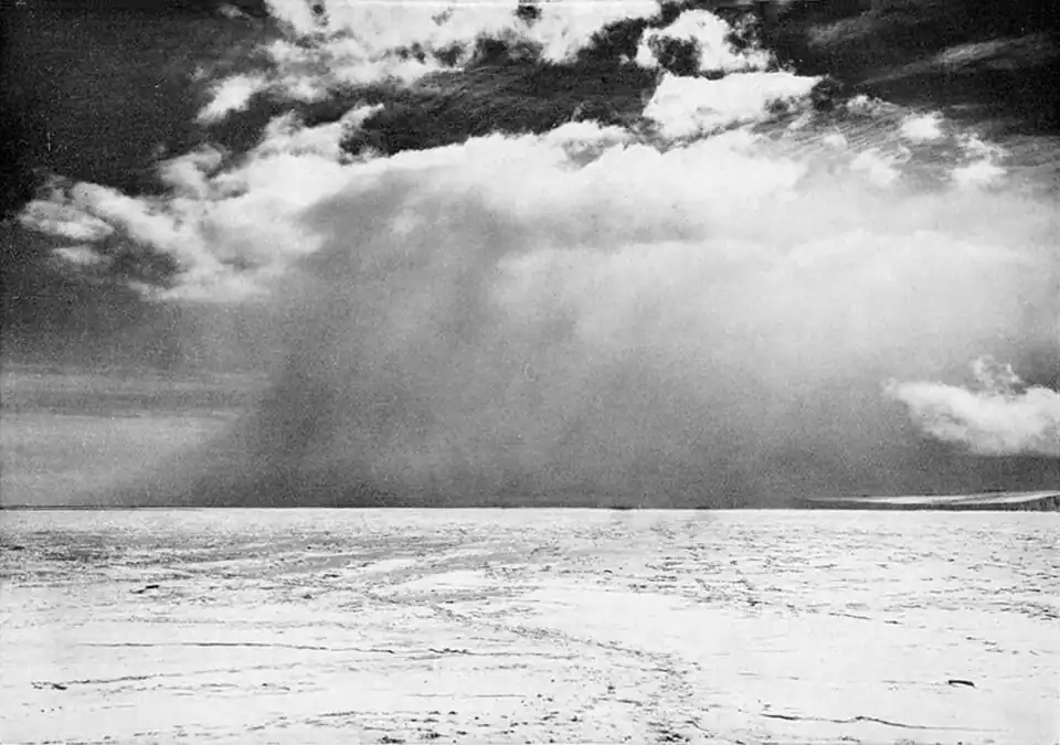 Photo of a distant cloud appearing to extend down to the surface of a frozen sea