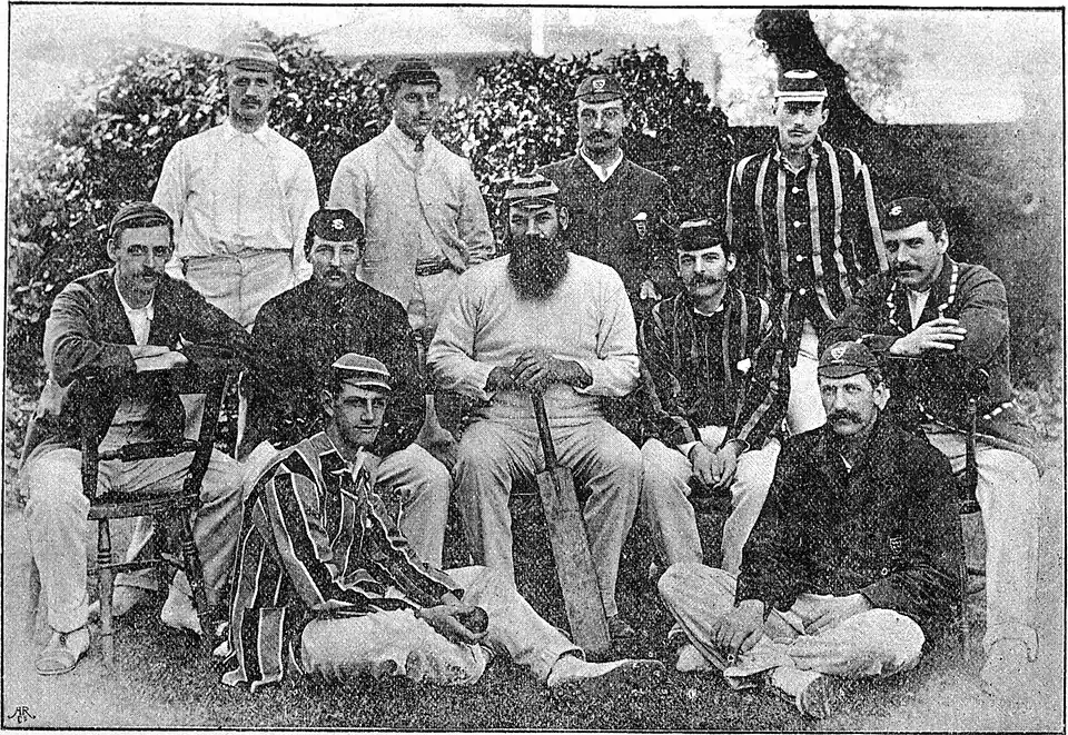 11 men dressed in cricket clothing posing for a group photograph. Three rows.