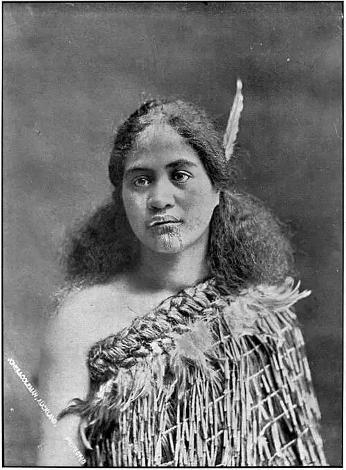 Māori woman in traditional costume with feather in hair and tattooed chin (moko kauae)