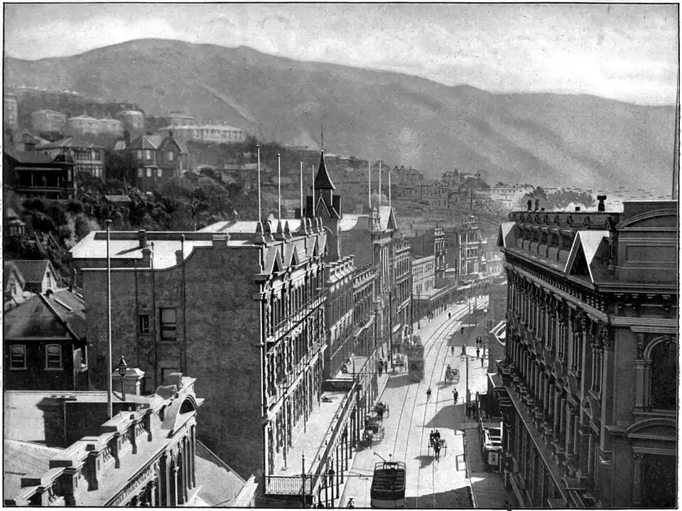 Road with taller buildings either side (three and four stories high), trams and tram lines, with houses on the slope to the left and Te Ahumairangi Hill (formerly known as Tinakori Hill) in the background