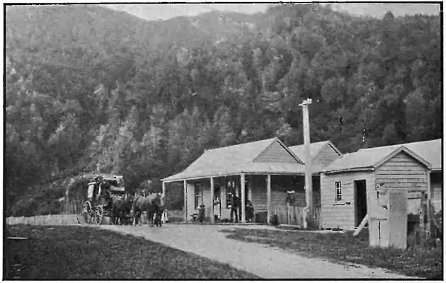Two buildings close together, with an extra two behind them. There is a group of people standing under the furthest building and next to a horse carriage