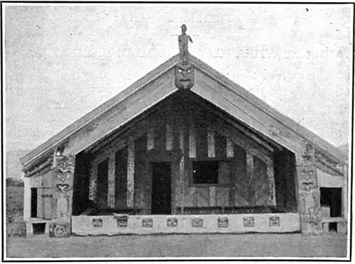 A wharenui or Māori meeting house with long bargeboards or maihi, carvings of ancestors, and a small door and window.