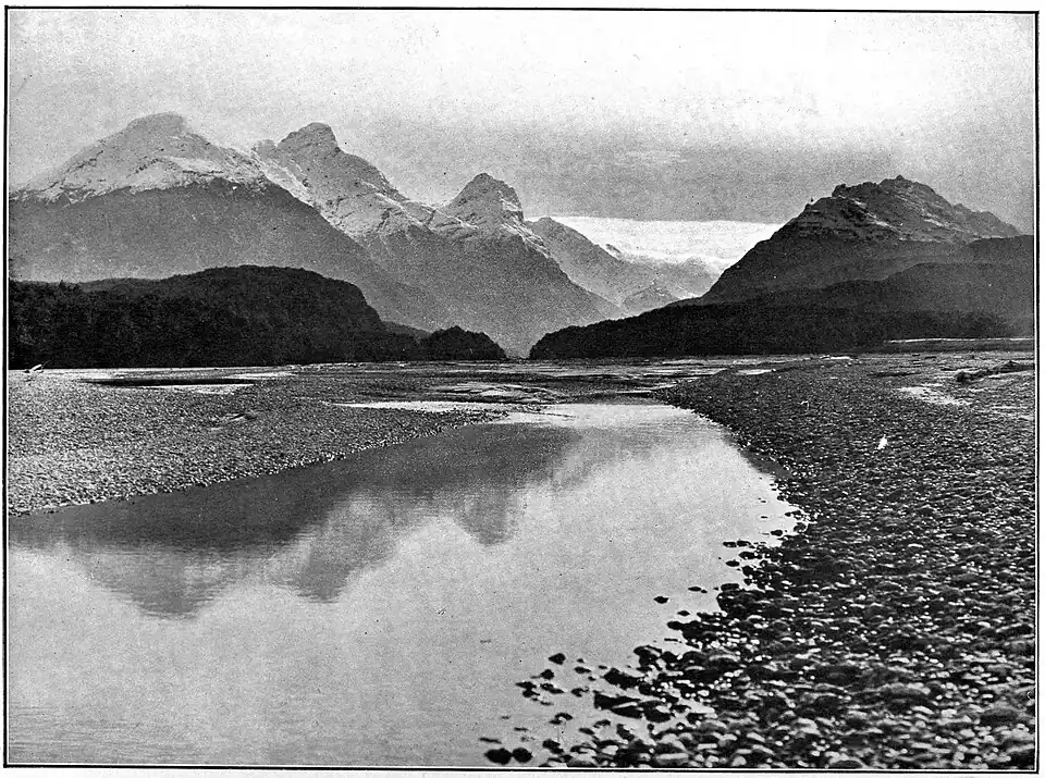 A lake with a stony shore and tall mountains in the distance.